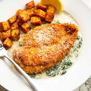chicken and creamed spinach on white plate with potatoes and silver fork