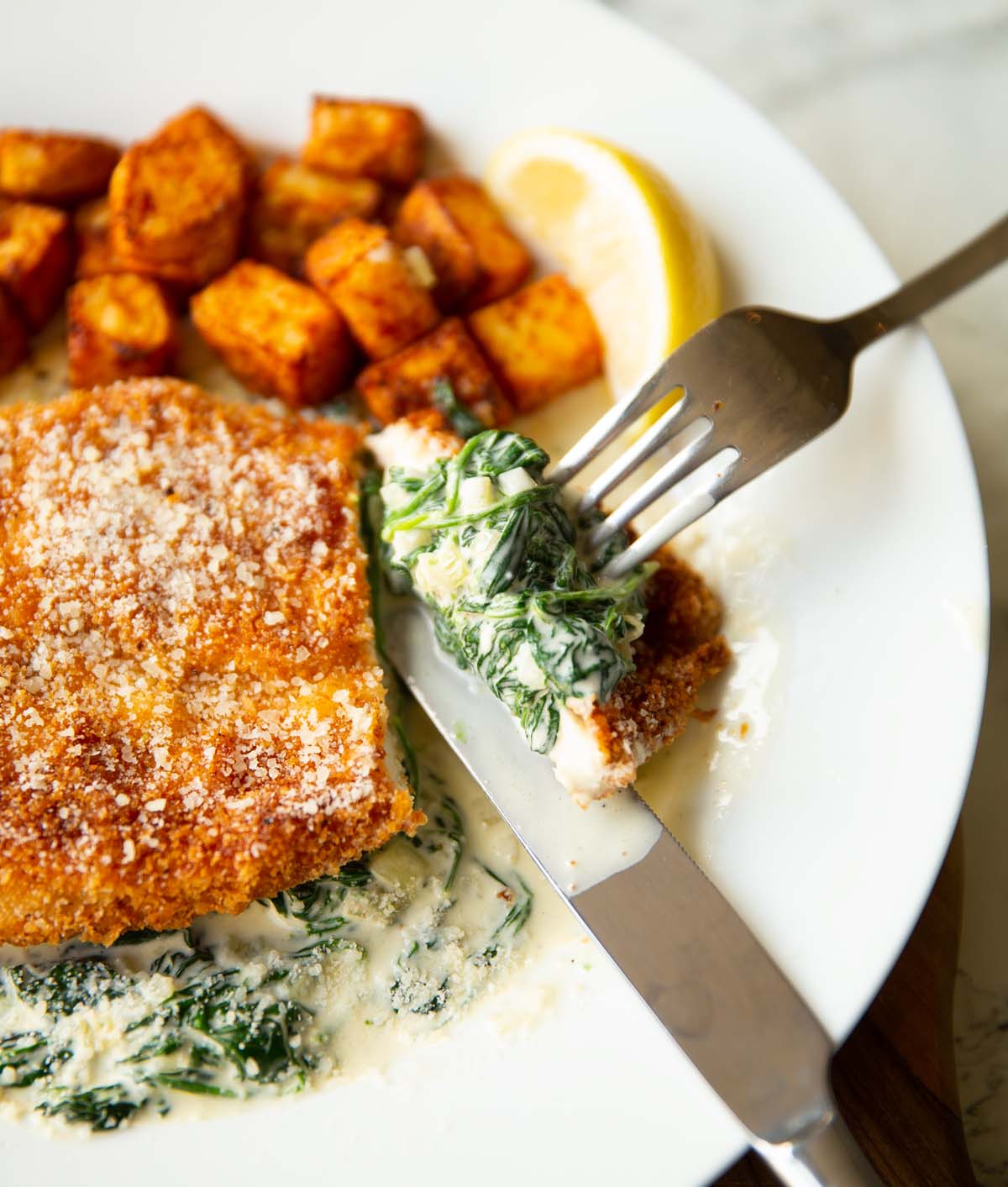 chicken and creamed spinach with silver fork cutting into on white plate